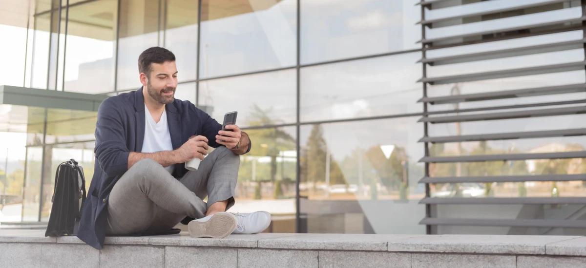 person sitzt draussen vor glasfassade und nutzt smartphone
